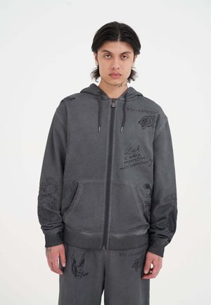 Grå zip-hoodie med detaljerede sorte grafiske designs, herunder dyr og tekst, med snoretræk i hætten og ribbede manchetter.