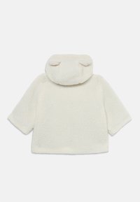 Kreemjas, kohev fleece'ist pullover, millel on ümar krae ja väikesed kõrva sarnased aksessuaarid kapuutsi peal. Omab laiu varrukaid ja pehmet tekstuuri.