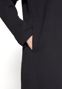 Czarna sukienka z miękkiego materiału, z długimi rękawami, boczną kieszenią i luźnym krojem. Czyste linie i minimalistyczny design.