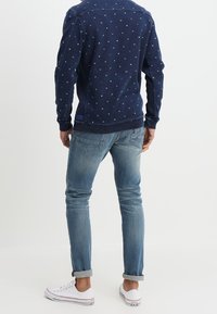 Svetrovka v námořnické modři s jemným vzorem teček, kombinovaná se světlými, slim-fit džíny a bílými teniskami, s ohrnutými rukávy.