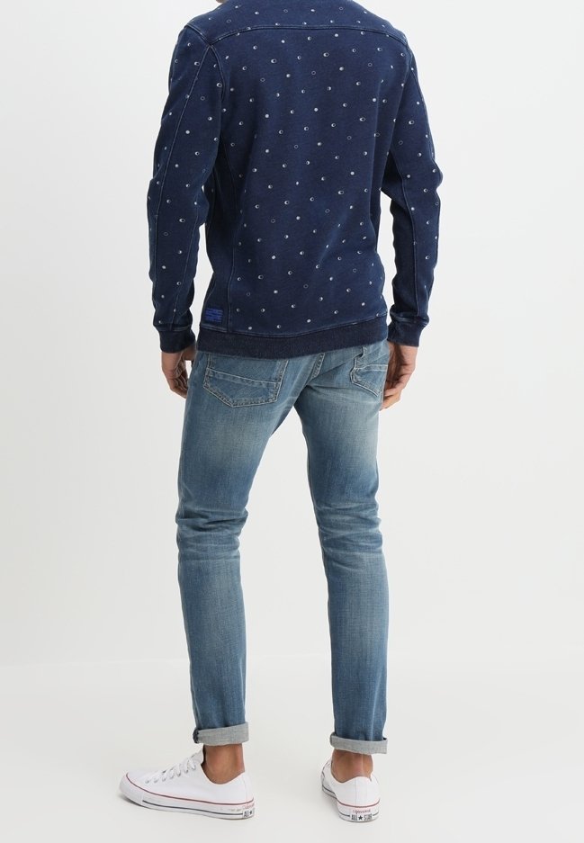 Svetrovka v námořnické modři s jemným vzorem teček, kombinovaná se světlými, slim-fit džíny a bílými teniskami, s ohrnutými rukávy.