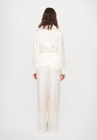 White sheer outfit featuring a textured floral pattern, long sleeves, and loose-fitting pants with a slightly cinched waist.
