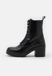 Bottine noire à lacets avec un motif croco texturé, talon bloc épais et semelle en caoutchouc. Dotée d'une languette à l'arrière du talon.