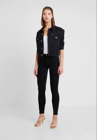 Svart denim cropped jakke, hvit tettsittende topp, svarte skinny jeans og gule hæler med stropper. Enkelt design med metallknapper og lommer.