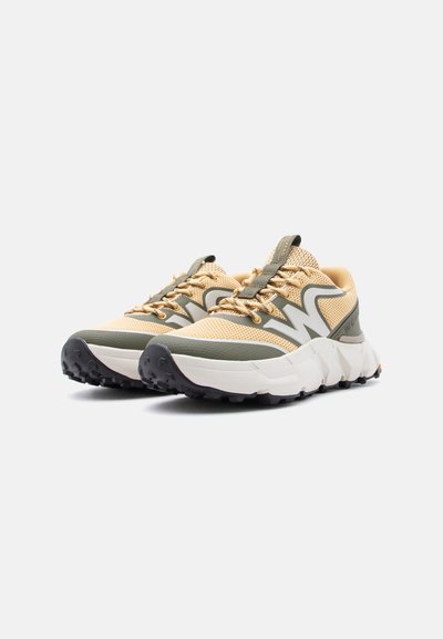 Ζευγάρι αθλητικών παπουτσιών σε μπεζ και πράσινο χρώμα με χοντρή λευκή σόλα και μαύρο πέλμα, τοποθετημένα σε απλό λευκό φόντο.