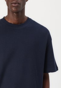 Tricou bleu marin cu mânecă scurtă, din bumbac texturat. Are un guler tip crew și o croială relaxată, cu un finisaj neted. Fără modele vizibile.