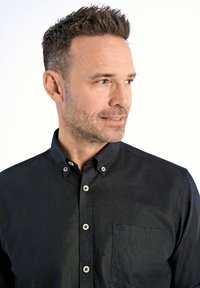 Camicia nera con bottoni in tessuto testurizzato, caratterizzata da un colletto classico, taschino frontale e bottoni rotondi con finitura metallica.