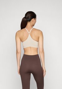 Bralette desportivo bege com design de costas nadador, apresentando alças finas e uma textura suave, combinado com leggings caneladas de cor castanha escura.