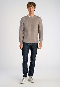 Ljusgrå ribbad stickad tröja med rund halsringning, bärs med mörkblå jeans och vita träningsskor. Slät textur, figurnära design.