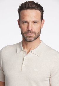 Beige kortärmad polotröja med klassisk krage, tre knappar och en liten broderad logotyp. Tillverkad av ett mjukt, slätt tyg.