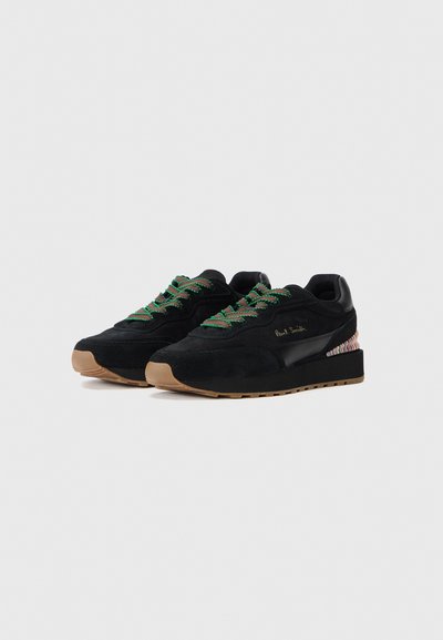 Sneaker in suede nero con lacci verdi, dettagli in pelle e un tallone decorato. Presentano una suola in gomma piatta e un design mid-top.
