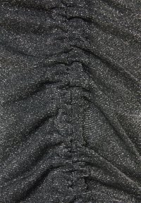 Tissu extensible noir avec des fils argentés scintillants, présentant une texture plissée et des plis sur toute la surface.