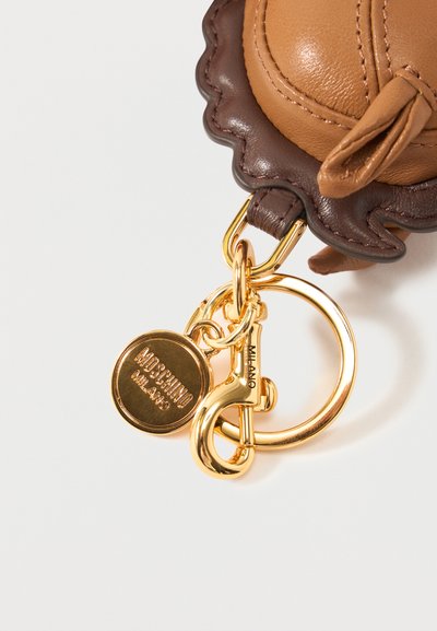 Barna bőr erszény hullámos szélű, arany kulcstartóra és kapocsra erősítve, kerek Moschino Milano logós charm díszítéssel.
