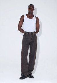 Tummanharmaat leveälahkeiset farkut normaalilla vyötäröllä, yhdistettynä valkoiseen toppiin. Malli seisoo käsivarret lanteilla, jalassa mustat kengät.