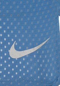 El tejido atlético azul presenta un diseño de malla con pequeños agujeros. Incluye un logo de Nike plateado. Textura suave con costuras reforzadas.