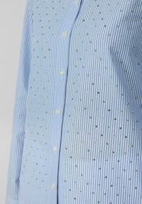 Blau-weiße gestreifte Button-up-Bluse, die mit kleinen Strasssteinen verziert ist, die in einem verstreuten Muster über den Stoff angeordnet sind.