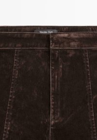 Tessuto di corduroy marrone scuro con righe verticali, caratterizzato da una vita e un'etichetta con la scritta "Massimo Dutti". Texture liscia e design strutturato.