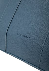 Superficie in pelle blu testurizzata con bordi cuciti e "GERRY WEBER" Impressa al centro.