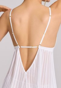 Biała odzież z cienkimi ramiączkami, z plecionym wzorem, złotymi akcentami i głębokim dekoltem na plecach. Tkanina ma pionowy prążkowany wzór.