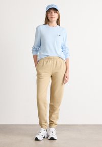 Ljusblå långärmad tröja med ribbade mudd, ihopparad med beige joggingbyxor med elastisk midja och vita sneakers med svarta detaljer.