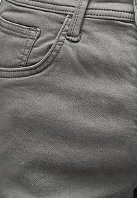 Gray denim fabric with a smooth texture, featuring a side pocket and visible stitching details, emphasizing a fitted design.