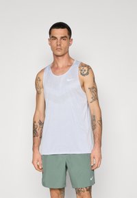 Weißes Nike-Tanktop mit strukturiertem Muster, runder Halsauschnitt und ärmellosem Design. Getragen mit grünen Shorts. Minimalistischer Stil.
