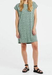 Mintgrön klänning med lös passform, korta ärmar, svarta prickar och rak fåll. Bärs med svarta sandaler med remmar.