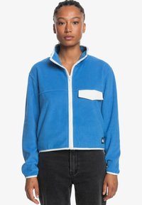 Blue fleece jacket with a white zip, high collar, and a white pocket. Cropped design with contrasting trim and logo at the hem.