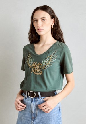 Zelené bavlnené tričko s V-výstrihom, ktoré má výšivky krídel v zlatej a striebornej farbe a nápis "Rock 'n' Roll". Skombinované s svetlo modrou džínsovou sukňou.