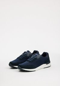 Zapatillas deportivas azul marino con parte superior de malla y tela, puntera reforzada, cordones y suela de goma blanca; presentan un patrón texturizado y un cuello acolchado.