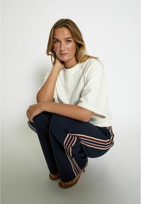 White relaxed fit t-shirt with short sleeves, paired with navy pants featuring red and white vertical stripes and brown sandals.