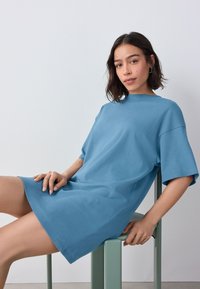 Rochie tricou din bumbac albastră, cu mâneci scurte, croială lejeră și decolteu rotund. Textură netedă și design simplu.