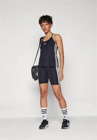 Černé sportovní tílko s třemi bílými pruhy, doplněné černými kraťasy s bílými postranními proužky. Černé tenisky a pruhované ponožky.