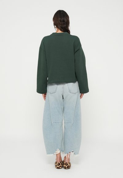 Πράσινο κοντό φούτερ με φαρδιά μανίκια συνδυασμένο με ανοιχτό μπλε φαρδιά τζιν παντελόνια με ξεθωριασμένα τελειώματα. Παντόφλες με λεοπάρ σχέδιο ολοκληρώνουν το ντύσιμο.