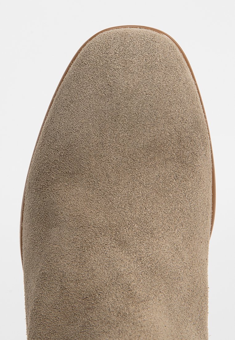 Beige Wildleder-Ankle-Boot mit glatter Textur, abgerundeter Zehe und minimalen Nähdetails, ausgestattet mit einer hellbraunen Gummisohle.