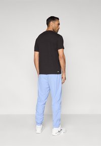 Μαύρο μπλουζάκι με κοντά μανίκια συνδυασμένο με ανοιχτό μπλε, ελαστικό παντελόνι φόρμας με λάστιχο στο τελείωμα, φορεμένο με λευκά αθλητικά παπούτσια. Απλός σχεδιασμός, casual εφαρμογή.