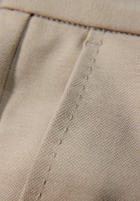 Beige stof met zichtbare stiksels en plooien, met gedetailleerde textuur en draadpatronen op geweven materiaal.