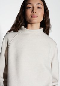 Maglione leggero beige, texture morbida, colletto alto e maniche raglán. Design semplice senza modelli o accenti visibili.