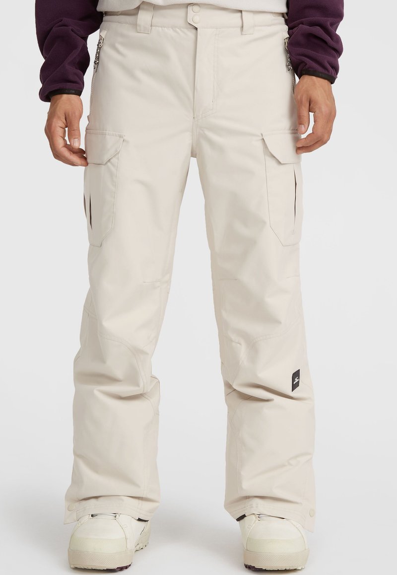 Beige snow pants featuring a loose fit, multiple side pockets, and reinforced stitching. Material appears water-resistant with a smooth texture.