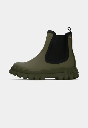 Olīvzaļas ūdensizturīgas potīšu zābaki ar teksturētu augšdaļu, melnām elastīgām sānu paneļiem un masīvu zoli ar izteiktu protektoru.