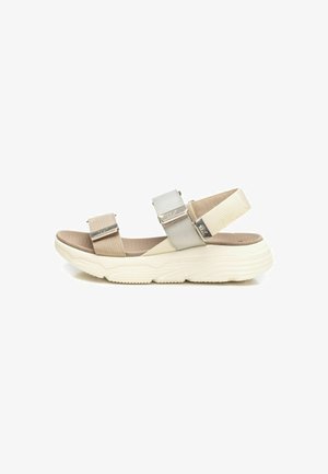 Sandalias beige y gris claro con correas texturizadas y herrajes plateados sobre una suela blanca gruesa. Diseño plano con punta y talón descubiertos.