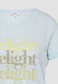 T-shirt à manches courtes bleu clair avec "delight" imprimé trois fois en jaune et beige, étiquette de marque s.Oliver et taille 36 visible au niveau du col.