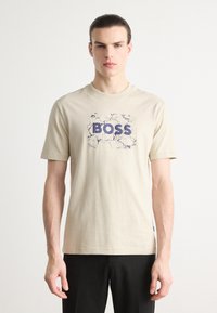 Beige bavlněné tričko s prasklým grafickým vzorem a výrazným textem "BOSS" v námořnické modři, krátké rukávy a kulatý výstřih.