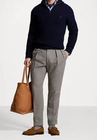 Mörkblå stickad tröja, ljusblå skjorta med prickar, grå veckade byxor, brun läderhandväska och bruna mockaloafers.