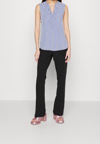 Top sans manches rayé bleu et blanc avec un col en V, associé à un pantalon noir ajusté et des sandales à talons blocs roses brillantes.