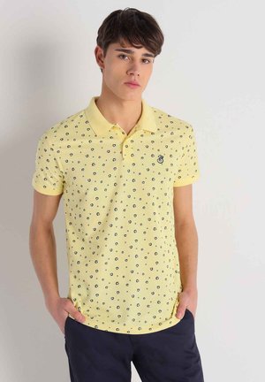T-shirt polo jaune avec de petits motifs circulaires bleu marine, à manches courtes et col classique. Présente un petit logo sur la poitrine gauche.