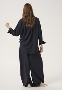 Cămașă oversized cu dungi bleumarin, dotată cu manșete cu nasturi; asociată cu pantaloni largi asortați. Țesătura pare netedă și ușoară.