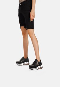 Sneaker sportive nere con tomaia texturizzata, suola bianca e accenti marroni. Abbinati a shorts di jeans neri con bordi sfrangiati.