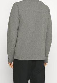 Graues Langarmshirt mit strukturiertem Strickmuster, Rundhalsausschnitt und geradem Saum. Dazu schwarze Hose getragen, was einen lässigen Look zeigt.