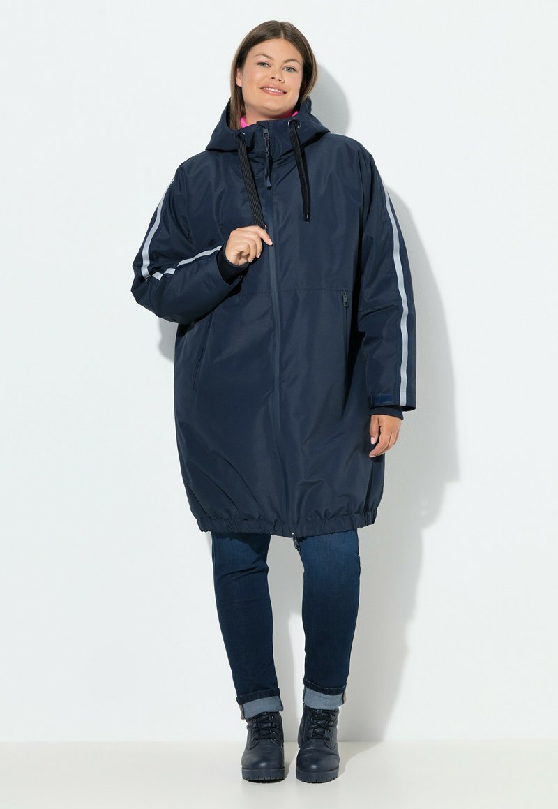 Parka azul marino impermeable con capucha, que presenta rayas plateadas en las mangas, dobladillo elástico y bolsillos frontales con cremallera. Textura suave.